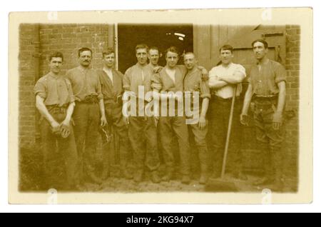 Original WW1 era postcard of cavalrymen of the 11th Hussars, (Prince Albert's Own also  known as the Cherry Pickers) posing for a relaxed, informal group photograph, in shirt sleeves, outside the stables after grooming their horses at Aldershot military training camp. The young man on very far LH of the group is Arthur Darling from Norwich, Norfolk. This was taken just before they were due to be transferred elsewhere, (possibly to York) later they may have been sent to join the battle at Messines) as infantry, not the cavalry. Location: Aldershot, Hampshire, England, UK. Circa October 1914. Stock Photo