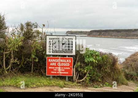 A sign warns of dangerous cliffs below and the closure of a walk on the firing range at Kimmeridge Bay, Dorset, UK. Stock Photo