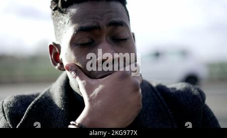 Preoccupied young black man. Anxious person sitting on the ground in city sidewalk Stock Photo