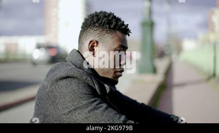 Preoccupied young black man. Anxious person sitting on the ground in city sidewalk Stock Photo