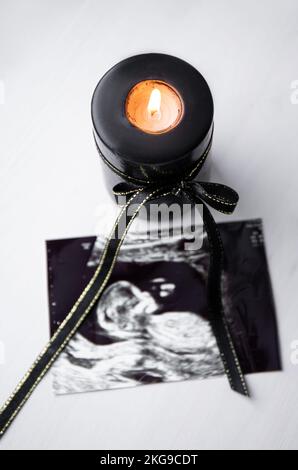 Conceptual image of mourning, miscarriage, pregnancy loss or grief counseling. Ultrasound picture of baby next to black candle with black ribbon burni Stock Photo