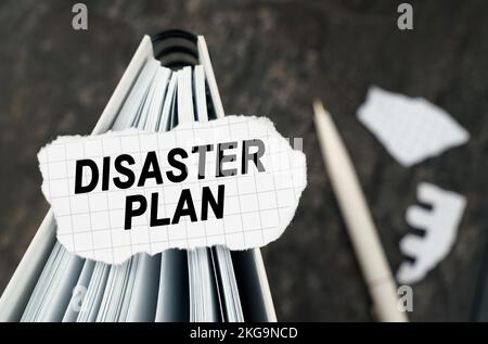 On the table is a notebook on which lies a piece of torn paper with the inscription - Disaster Plan. The pen lies outside the sharpness zone. Stock Photo