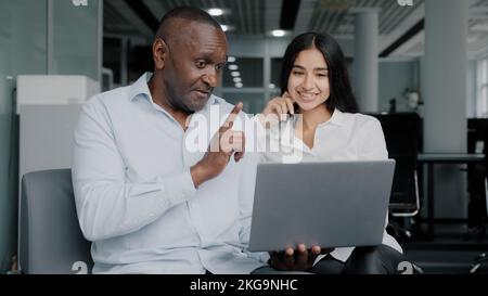 Diverse colleagues two business partners african arabian co-workers discuss internet project on laptop at office meeting planning working main tasks Stock Photo