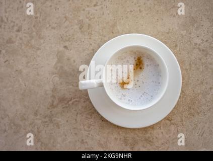 A white cup of frothed coffee on a beige marble table. Coffee cup top view. Creme beige coloring. Stock Photo