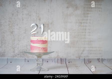 21st Birthday cake pink and silver cake with some sprinkles and 21st candlelight on a white wooden background. Stock Photo