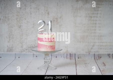 21st Birthday cake pink and silver cake with some sprinkles and 21st candlelight on a white wooden background. Stock Photo