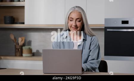 Caucasian elderly female businesswoman freelancer granny shopper buyer work on laptop from home rejoice victory win online lottery discounts in Stock Photo