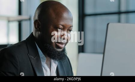 Focused african entrepreneur typing on keyboard working distantly in office look at monitor studying online course develop business startup american Stock Photo