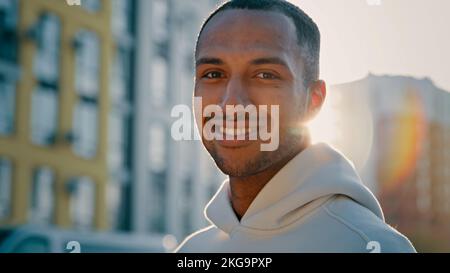 Close up male portrait in morning sun rays young athletic handsome afro american latino guy stand on city street alone successful millennial sportsman Stock Photo