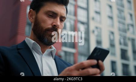 Male businessman texting messages on mobile phone chatting online search information read notification caucasian 30s man freelancer work in city with Stock Photo