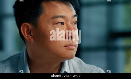 Businessman employer ethnic asian korean man sit alone in office thoughtful looking at window planning business idea turning head to camera smiling Stock Photo