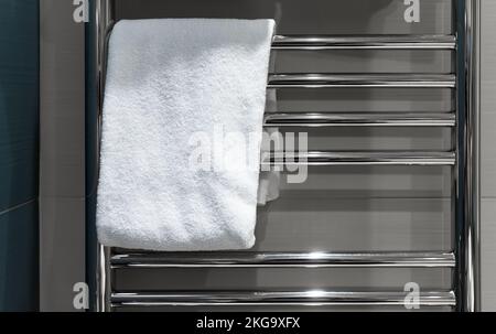 White towel hangs dried on a heated towel rail in the bathroom Stock Photo