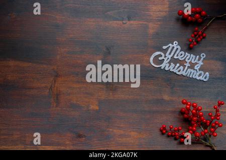 poster with the text merry christmas in silver glitter on a dark wooden background with red berry branches Stock Photo