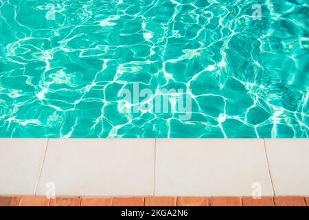 Swimming pool border. Close up edge of white cement floor near swimming pool with clear blue water. Stock Photo