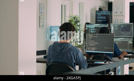Multiethnic group of programers working on server code to develop new database user interface on computers. IT engineers coding html script with artificial intelligence on terminal window. Stock Photo
