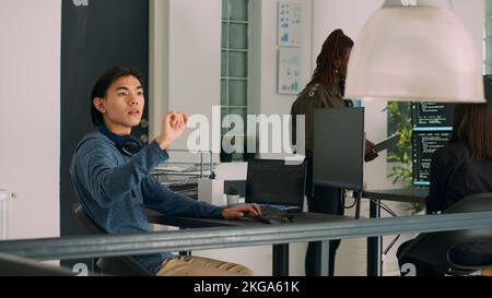 Programer typing source code on computer and turning head to use ar hologram, wokring with augmented reality and html script. Software engineer checking holographic database writing ai algorithm. Stock Photo