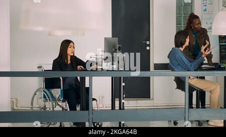 Asian system engineer with impairment programming app script on terminal window, using big data language. Developer in wheelchair working with cloud computing database, firewall security. Stock Photo