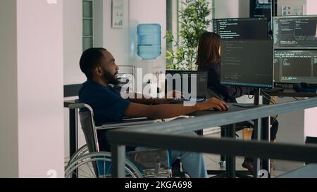 Software developer wheelchair user working on html script code, checking database and server to develop app system. Coder with chronic impairment using programming source in it office. Stock Photo