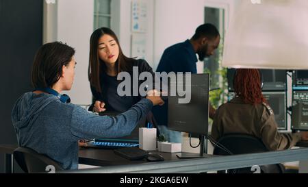 Asian team of IT engineers analyzing html code on terminal window, using server database on computer. Coders talking about programming language and cloud computing user interface. Stock Photo