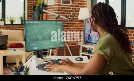 Female freelancer looking at annual sales report on computer, analyzing accounting data statistics on web. Woman working remote with financial diagrams, marketing education at home. Stock Photo