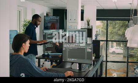 Diverse team of database developers analyzing code on terminal window, working with html script and artificial intelligence. System engineers talking about app developing interface. Stock Photo