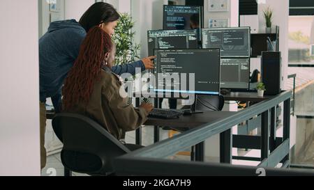 Diverse team of ai cloud programers talking about coding script in front of computer, working on server interface development. Programmers doing teamwork to plan html software language. Stock Photo