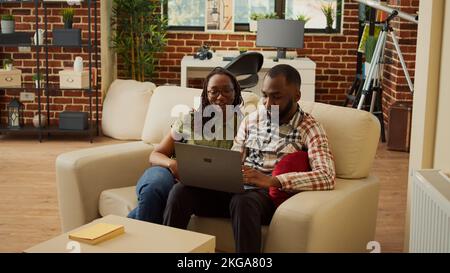 Boyfriend and girlfriend watching online videos on laptop, relaxing together on couch and having fun. Browsing internet on pc and enjoying leisure activity, laughing staying at home. Stock Photo