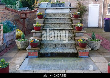 beautiful steps waterfall in a garden with symmetrical potted plants on each side Stock Photo