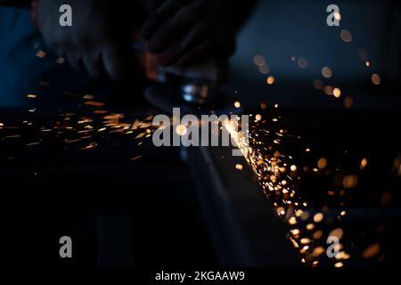 Sparks in dark. Metal grinding. Orange lights fly in different directions. Work in metal workshop. Steel processing with grinder. Background of many s Stock Photo