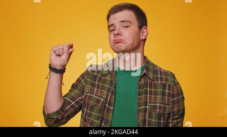 Need some more, please give me. Man showing a little bit gesture with sceptic smile, showing minimum sign, measuring small size, asking for help. Young boy isolated alone on yellow studio background Stock Photo