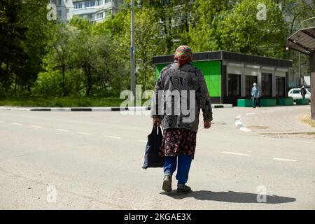 Russian pensioner walks down street. Married in old clothes. Poor life. Elderly woman crosses road. Stock Photo