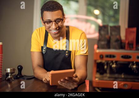 Cheerful coffee shop worker using a gadget in the workplace Stock Photo