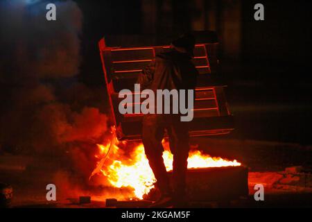 Nablus, Palestine, 22/11/2022, A Palestinian demonstrator add a wooden pallet to fuel the flames of fire while blocking the road leading to Joseph's Tomb in the city of Nablus in the occupied West Bank. Demonstrators made a bold move to prevent Israeli settlers from going to Joseph's Tomb after staging demonstrations, attacking Palestinian property, and closing the streets surrounding the city of Nablus. This tomb has long been at the center of conflict between Jews, Christians, and Muslims. Some Jews believe that Biblical Joseph is buried in the grave; Muslims believe that Sheikh, an Arab lea Stock Photo