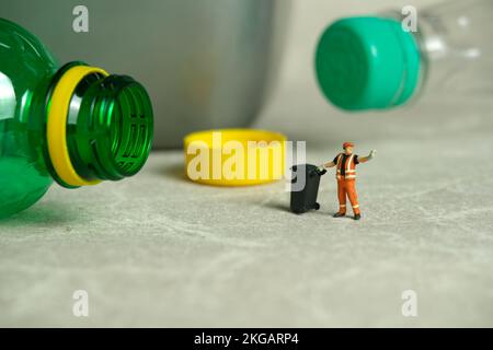 Miniature people toy figure photography. Cleaning workers walk among plastic drink bottles scattered on the floor near the trash can. Image photo Stock Photo