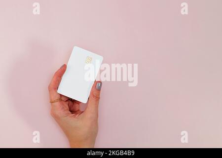 Woman's hand holding white plastic credit or debit card with chip over the pink background Stock Photo