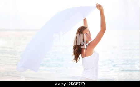 Frolicking in the fresh sea breeze. Young beauty waves her sarong in the ocean breeze at sunset. Stock Photo