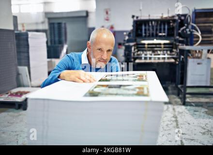 Getting a different angle on the issue. a man checking the quality of a print run in a factory. Stock Photo
