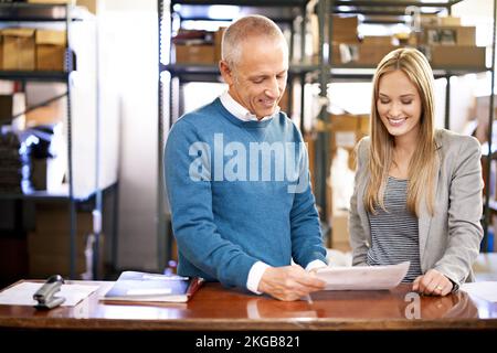 Weve moved a lot of orders today. a two managers looking through paperwork on the warehouse floor. Stock Photo