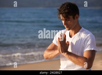 Connecting with mother nature. a young man doing yoga at the beach. Stock Photo