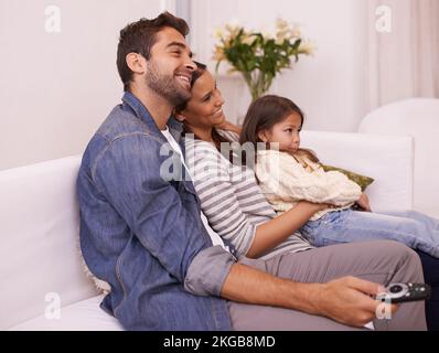 Lets watch some cartoons. a young family sitting together on a sofa watching television. Stock Photo