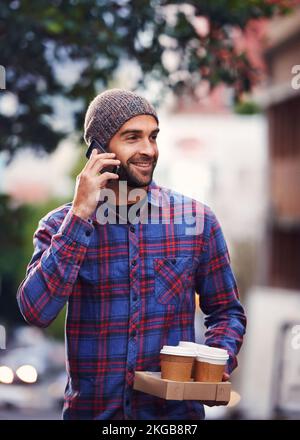 Im bringing coffee. a handsome young man in winter wear talking on his mobile phone while holding cups of coffee. Stock Photo