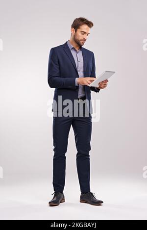 Reviewing the latest updates. Studio shot of a well-dressed man using a tablet against a gray background. Stock Photo