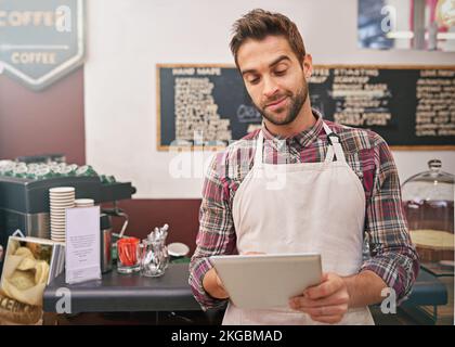 Ordering new stock online. a young male barista using his tablet in a coffee shop. Stock Photo