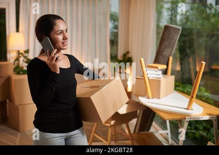Smiling woman packing belonging and ordering movers and van by phone Stock Photo