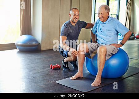 Theres no age limit on a healthy lifestyle. a senior man working out with the help of a trainer. Stock Photo
