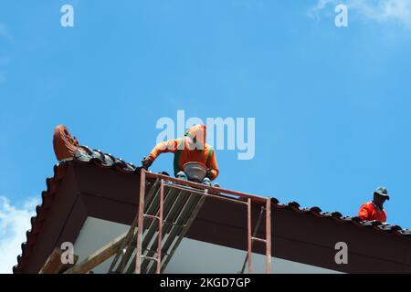construction workers fixing roof against clouds blue sky, install shingles at the top of the house. Renovate, painting the walls, improvement, build h Stock Photo