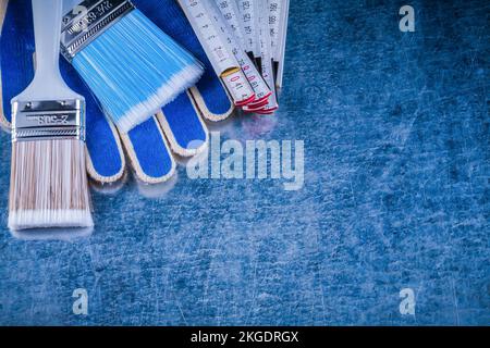 Composition of wooden meter paintbrushes safety gloves on metallic surface. Stock Photo