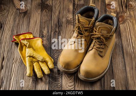construction safety tools yellow working gloves and leather working boots on vintage wooden background Stock Photo