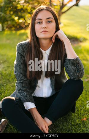 Front view of a successsful female freelancer sitting on green grass taking a break from work in open air. Concept of studying and learning material Stock Photo