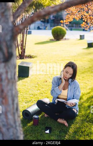 Happy brunette hair sporty woman resting after exercising in park, reading a book. Relax, lifestyle concept. Summer relaxation concept. Healthy Stock Photo